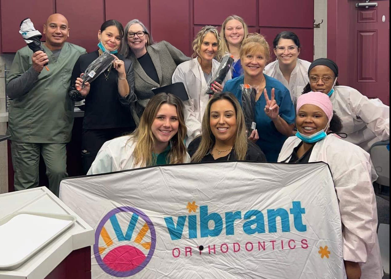 Vibrant Orthodontics team holding the practice banner at their orthodontic office in Tallahassee, FL